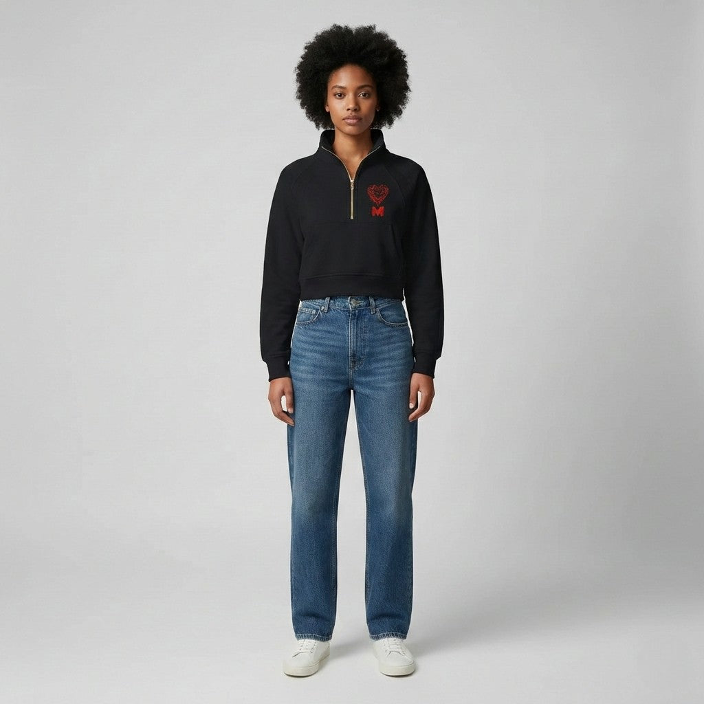 Person wearing a black sweater with a red heart design and blue jeans on a white background